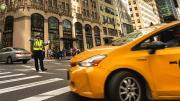 A yellow cab turns through an intersection directed by a police officer