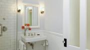 In an interior bathroom, transom windows and frosted glass allow natural light from an exterior window in the next room to reach the space. Allen chose to use period details such as wainscoting and molding to draw attention away from modern anachronisms like the frameless glass shower door. 