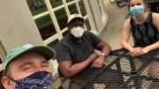 Photo of the author sitting with two friends, all in masks, in the Radcliffe Quadrangle as they watched virtual Commencement