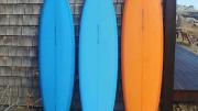 Two blue surfboards and an orange on rest on end against a weatherbeaten wall.