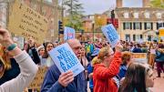 A crowd of marchers carry signs that read "We need a fair raise"