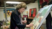 Surrounded by her own works, Langer wields a brush in her home studio.  A self-taught painter who took up the avocation in midlife, she describes her autodidactic approach to art in <em>On Becoming an Artist: Reinventing Yourself Through Mindful Creativity</em> (2005).