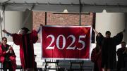 Danoff Dean of Harvard College Rakesh Khurana and Harvard Alumni Association president Vanessa Liu ’96, J.D ’03 unfurl the class of 2025 banner