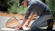 Gilens kneeling on a paved walkway in South Lake Tahoe, installing the artwork