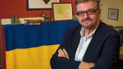 Serhii Plokhy in his Harvard office, smiling with his arms crossed. Behind him hangs a Ukrainian flag signed by Kyiv mayor Vitali Klitschko