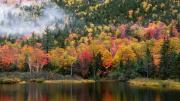 A lake next to a mountain with autumn foliage and fog