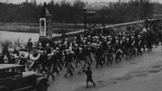 Band members wearing sailor hats march across a bridge to play at a football game