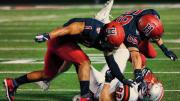 Two Harvard football players tackle a player from Brown.