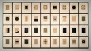 A grid of of 36 abstract black-and-white prints, each representing some aspect of the homes that artist Zarina has lived in, with Urdu and English inscriptions under each