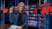 Amy Goodman featured in her broadcast studio giving the peace sign