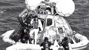 A man in a wetsuit helps an astronaut out of an Apollo capsule floating in the ocean