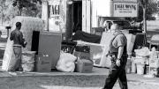 A deputy sheriff supervises as an evicted tenant carries belongings to the curb.