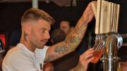 Handsome, tattooed bartender at Provincetown Brewing Company tapping craft beer for a customer