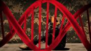 A double-helix image, in red, framing a man in military camouflage, crouched, seated, holding his head, and