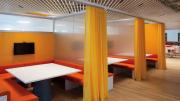 A centrally located 3,100-square-foot library has study carrels with orange benches, white desktops, and yellow privacy curtains.