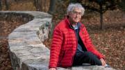 David Roberts seated outdoors on a stone wall by the Charles River