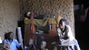 Bashir and Hajara Barigye with two of their children inside their old mud-walled house. Once their new brick house is complete, the old one will serve as a kitchen.