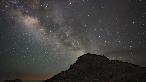 Star-filled night sky with the Milky Way arching over a rocky silhouette.