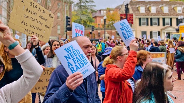 A crowd of marchers carry signs that read "We need a fair raise"