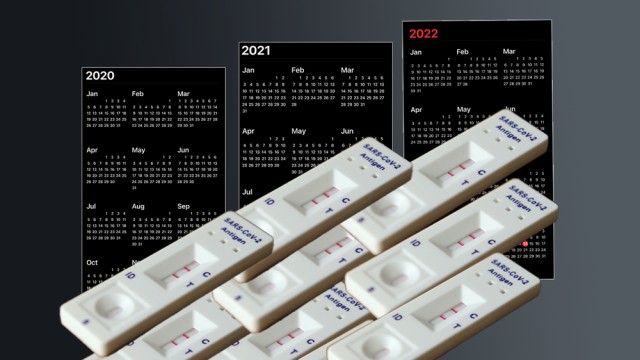 A stack of positive COVID tests in the foreground with 2020-2022 calendars in the background