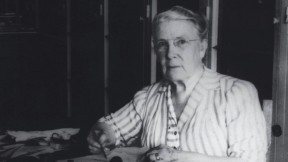 Photograph of a stout middle-aged woman seated at her desk, writing