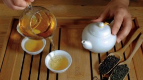 Hands pouring steeped golden-colored tea from a ceramic pot