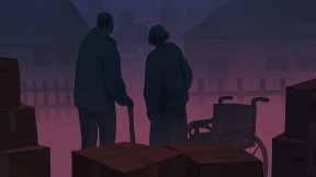 An elderly couple with infirmities stand on a sidewalk with their moving boxes