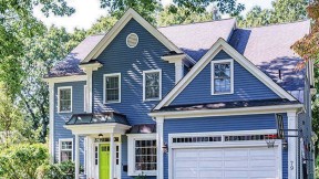 Exterior of blue house with garage surrounded by greenery