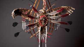 In Yup’ik lore, the crane—depicted in the mask above—connotes stealth, power, and insight. The human face on the bird’s belly represents its <em>yua,</em> or spirit—the part of the animal that understands, and can relate to, humans. The porcelain “teeth” that border the face are a reminder to use one’s innate gifts to good effect, or risk being consumed by them. The porcelain “bones” hanging from the wings ward off evil spirits; wooden rings represent this world and the spirit world.