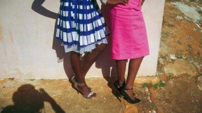The lower halves of two women stylishly dressed in bright colored skirts and high heels