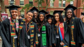 Harvard undergraduates standing happily in Commencement regalia 