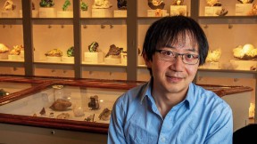 Roger Fu sits in front of a display case of rock samples