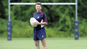 Holding a rugby ball, Sue Parker stands before rugby goalposts. She is Harvard&rsquo;s first varsity coach in the sport. 