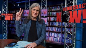 Amy Goodman featured in her broadcast studio giving the peace sign