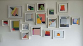 A collection of abstract geometric paintings hang above a white couch