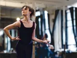 A dancer in a black leotard poses gracefully in a bright studio, with mirrors reflecting her movement.