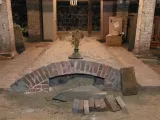 Brick archway with a sandy base, surrounded by wooden planks and boxes in a dim space.