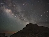 Star-filled night sky with the Milky Way arching over a rocky silhouette.