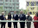 Several people are holding a large ribbon for a ceremony outside a modern building.