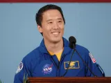 Smiling astronaut in blue jumpsuit speaking at a podium, colorful background.