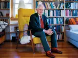 Harvey Mansfield seated in a bright yellow chair, surrounded by bookshelves and cozy decor.