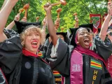 Graduates in caps and gowns celebrate joyfully, raising their hands in excitement.