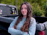 A woman with long hair stands confidently with crossed arms next to a pickup truck.