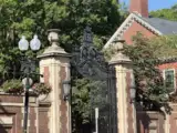 Morgan gate with brick pillars, surrounded by greenery and historic architecture.