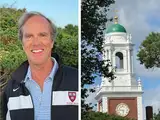 Smiling man in a Harvard jacket alongside a clock tower with green dome against the sky.