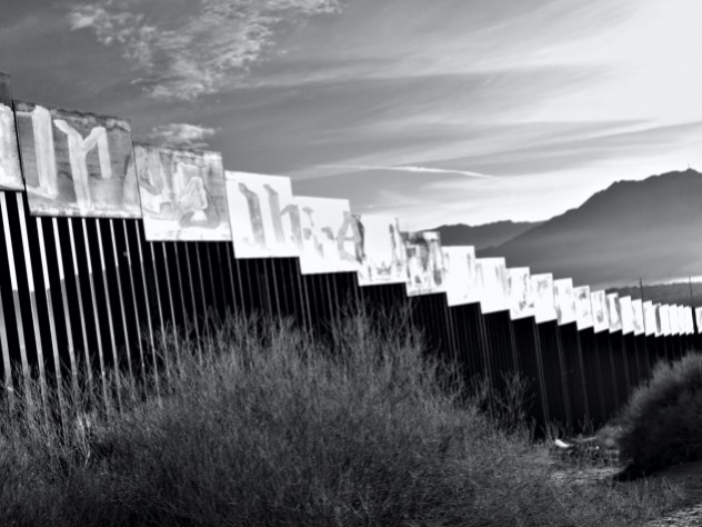 A photograph of the border wall stretching toward a mountain in the distance