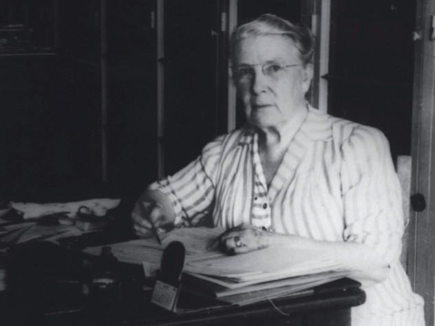Photograph of a stout middle-aged woman seated at her desk, writing