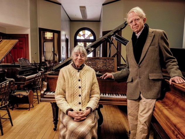 An older couple standing in a large room filled with pianos
