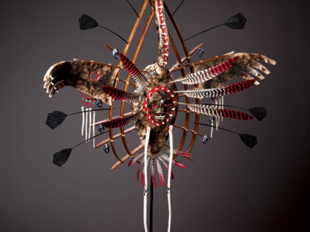 Courtesy of Santa Fe Indian Market-SWAIA In Yup’ik lore, the crane—depicted in the mask above—connotes stealth, power, and insight. The human face on the bird’s belly represents its <em>yua,</em> or spirit—the part of the animal that understands, and can relate to, humans. The porcelain “teeth” that border the face are a reminder to use one’s innate gifts to good effect, or risk being consumed by them. The porcelain “bones” hanging from the wings ward off evil spirits; wooden rings represent this world and the spirit world.