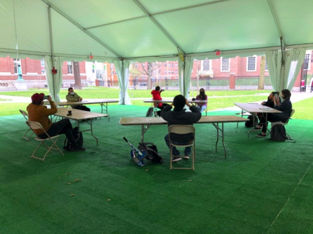 Students gather in desks under a tent, a pilot of outdoor instruction for performance-based courses